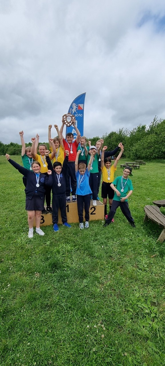 12 children in coloured tshirts with trophy on podium in a field